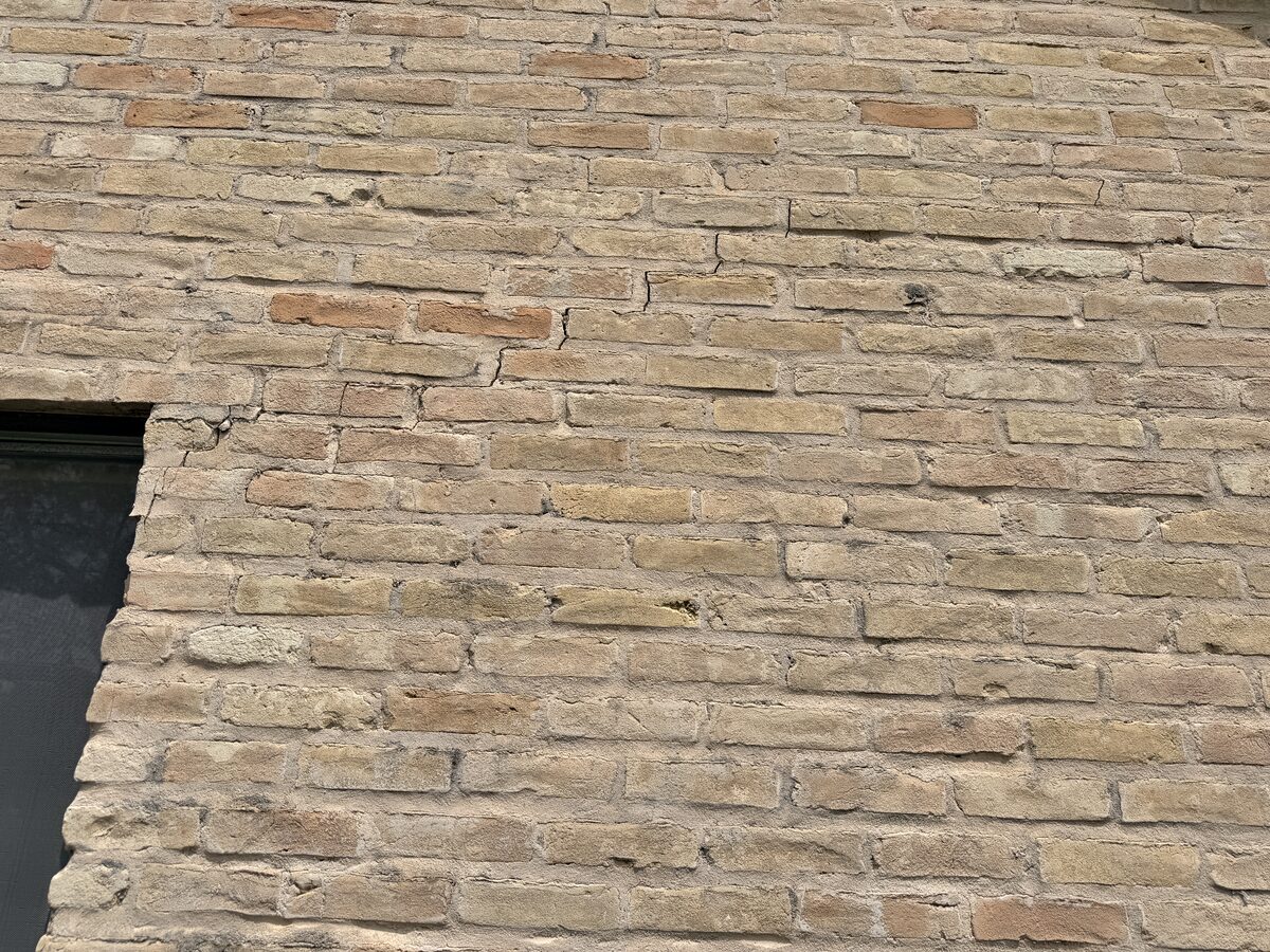 Stair-step cracking through brick mortar joints above a window corner caused by foundation settlement