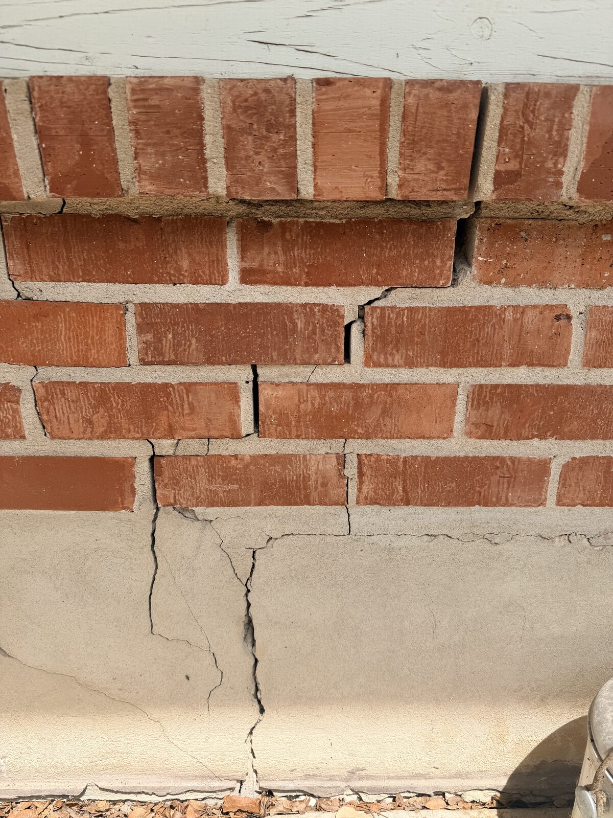 Stair-step cracks in red brick above a cracked concrete stem wall on a settling Central Texas home