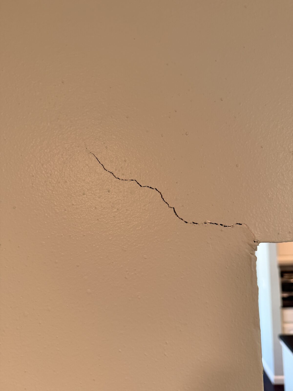 Stepped drywall crack angling down a wall into the top corner of a doorway opening