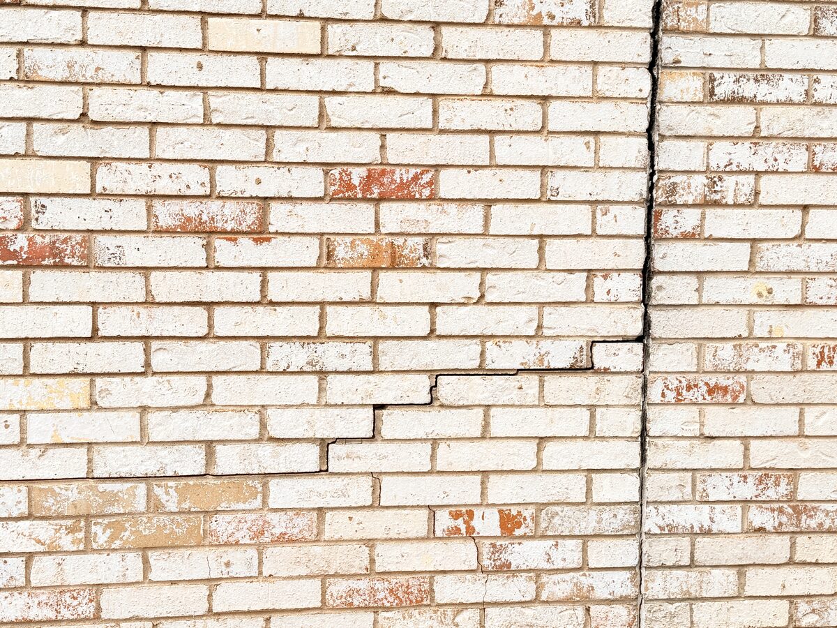 Stair-step crack in painted brick meeting a long vertical crack on a house exterior