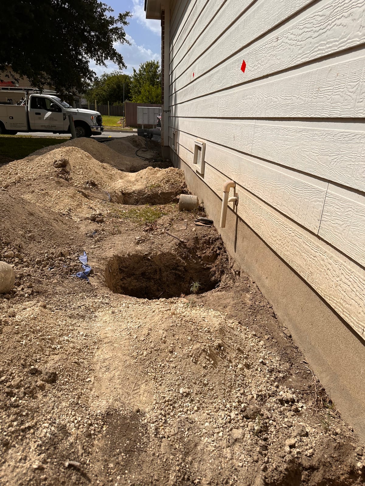 Excavation pits opened along a home's foundation perimeter in preparation for hybrid pier installation