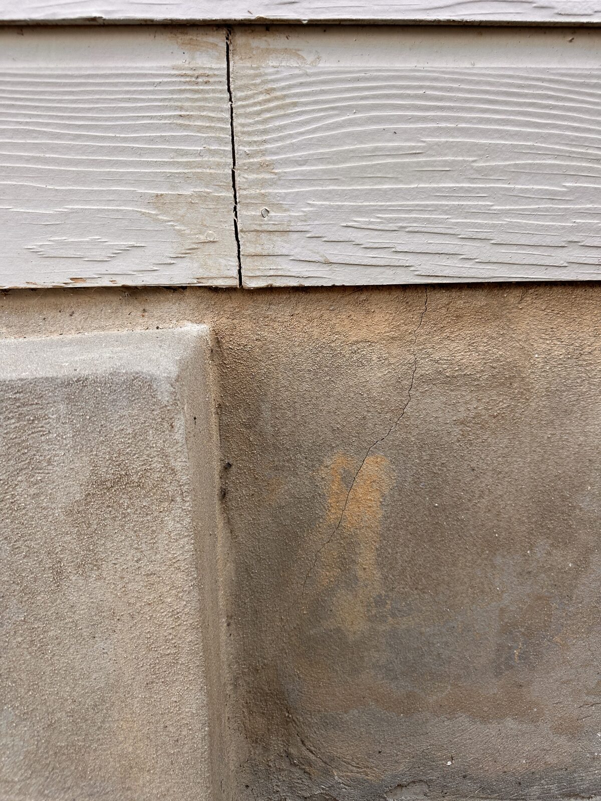 Corner of a parged concrete stem wall beneath fiber-cement siding during a foundation inspection