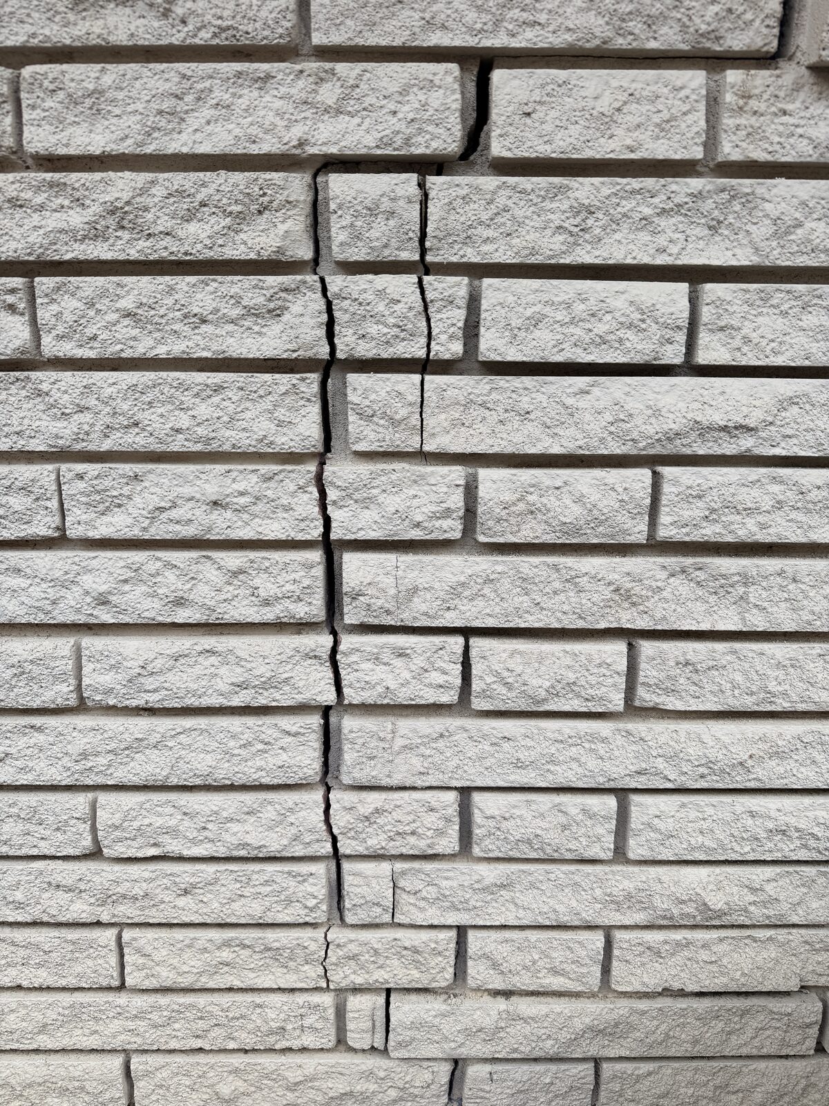 Closeup of displaced stone veneer blocks along a wide settlement crack before foundation repair