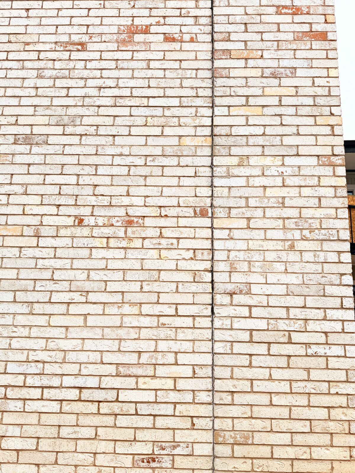 Straight vertical separation running the full height of a cream brick wall where two wall planes meet