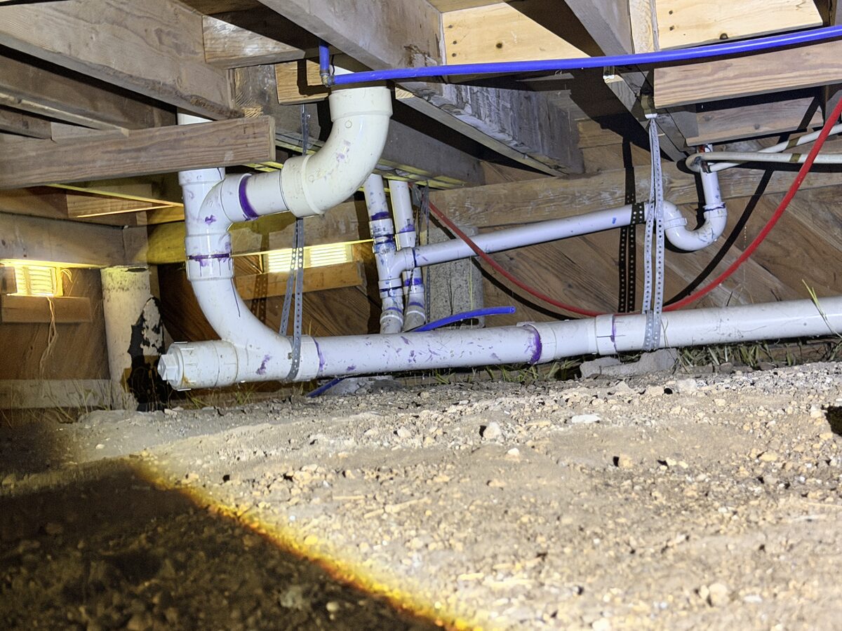 White PVC drain pipes hung on metal straps beneath wood floor framing
