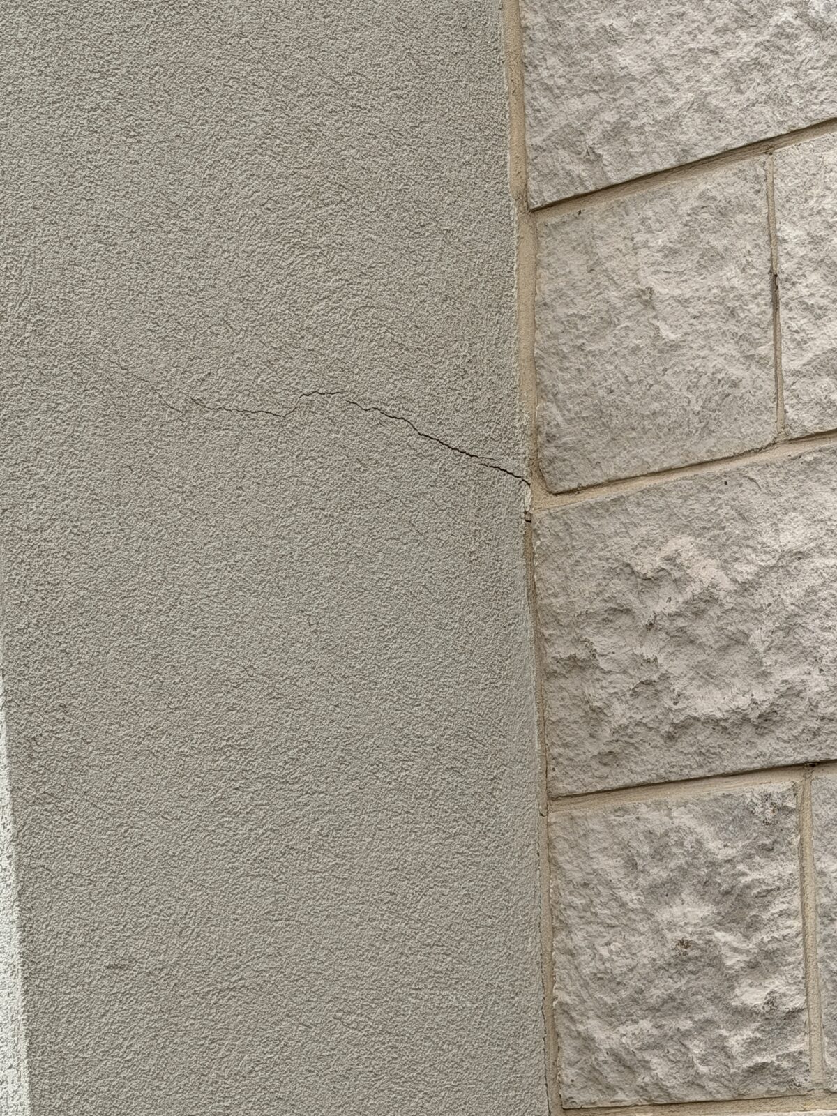 Hairline crack crossing stucco beside a split-face block column at a commercial building with foundation movement