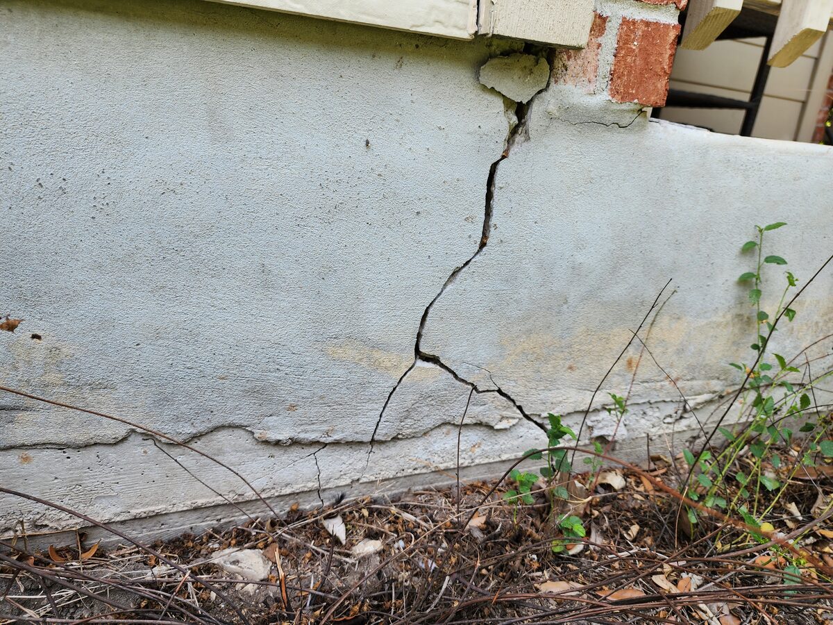Branching diagonal crack in a stucco-coated stem wall beneath brick veneer, an exterior sign of foundation settlement