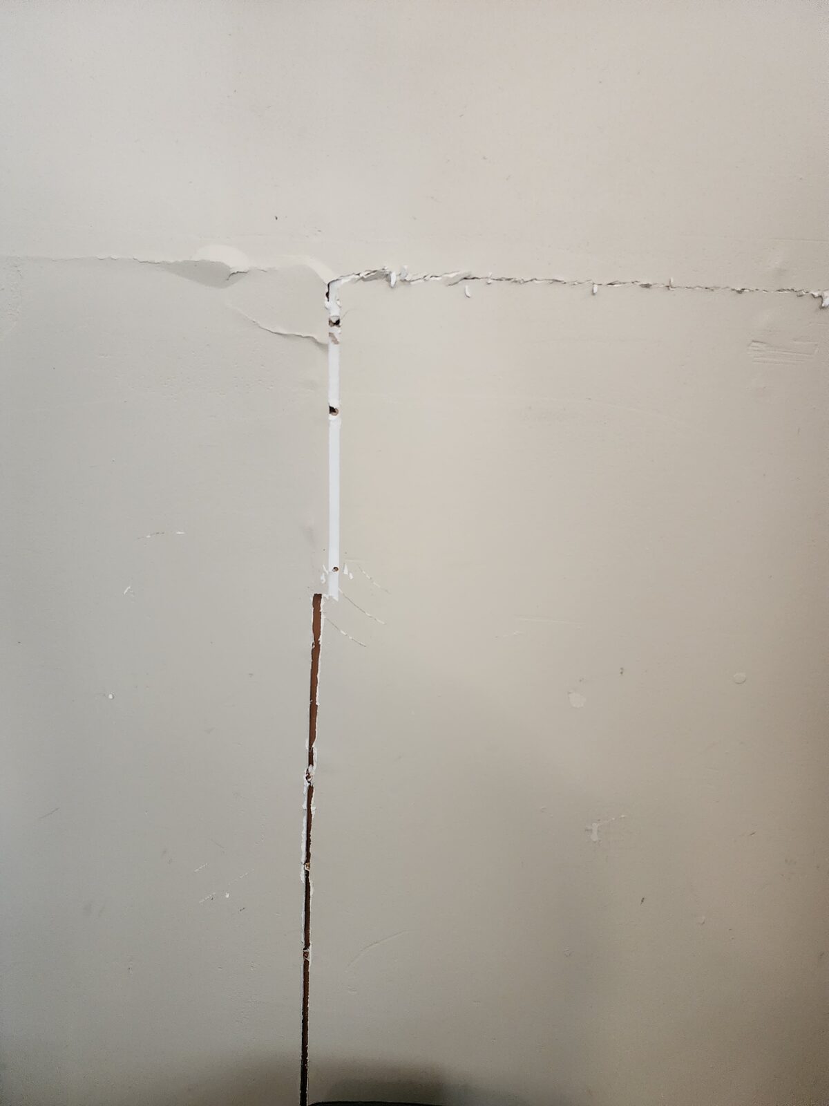 T-shaped crack where a vertical drywall seam meets a ceiling-line crack, a common symptom of foundation settlement