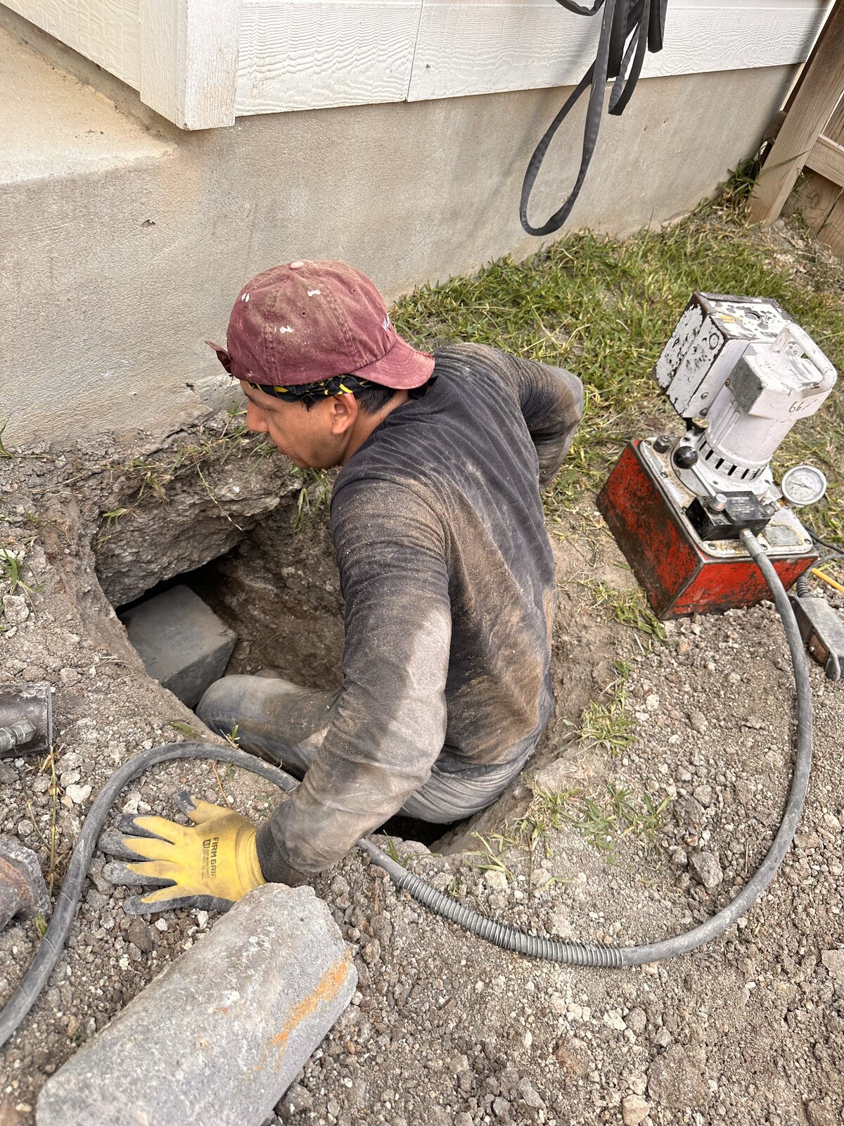 Technician working in a pier pit with a hydraulic pump beside the foundation wall during underpinning