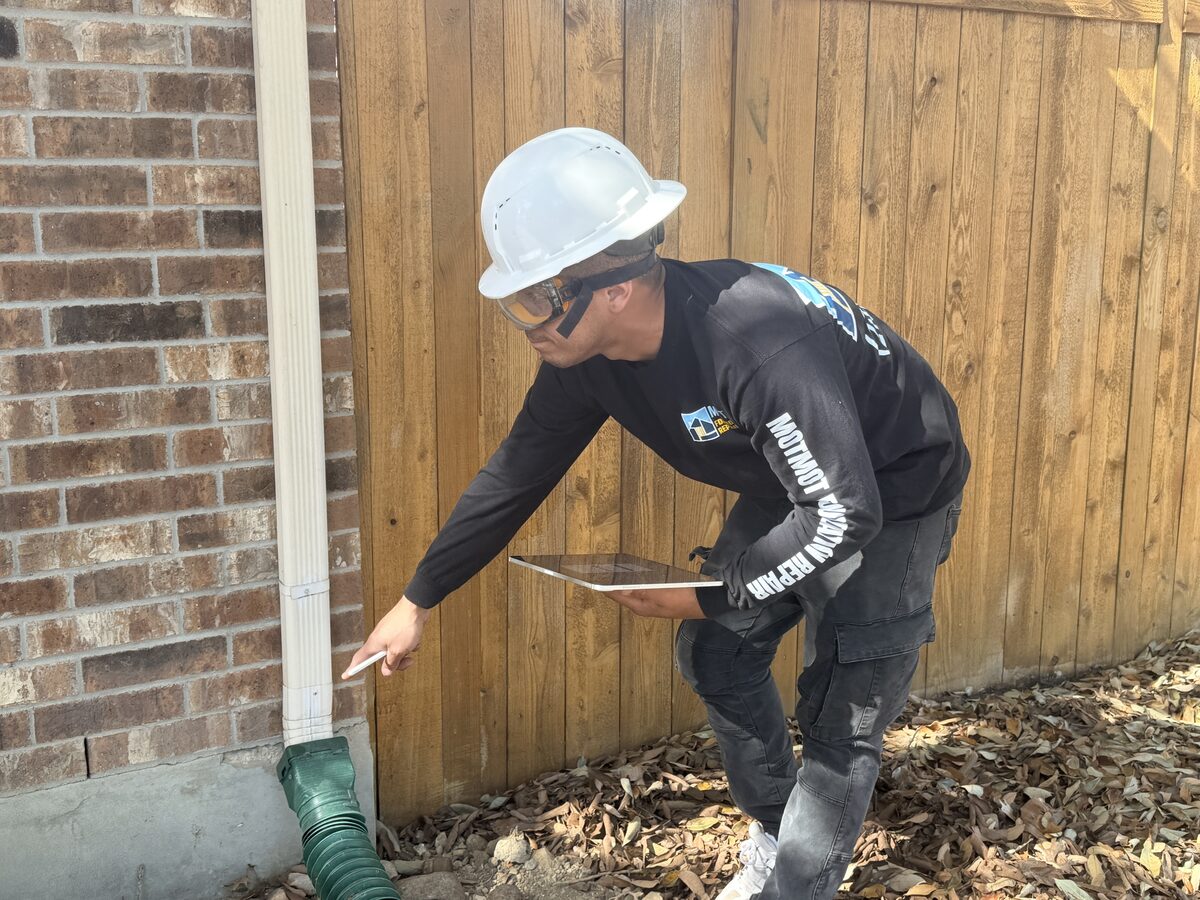 Motmot technician pointing out a downspout extension discharging away from a home's foundation edge
