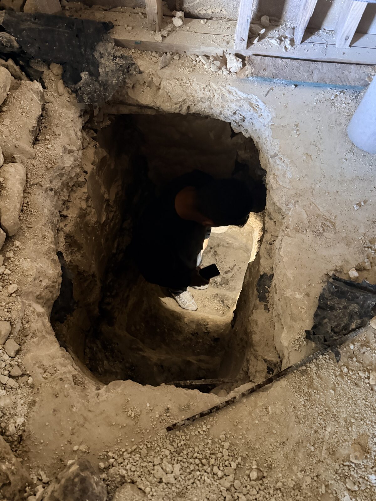 Technician working at the bottom of a deep hand-dug pier pit beneath a home's slab foundation