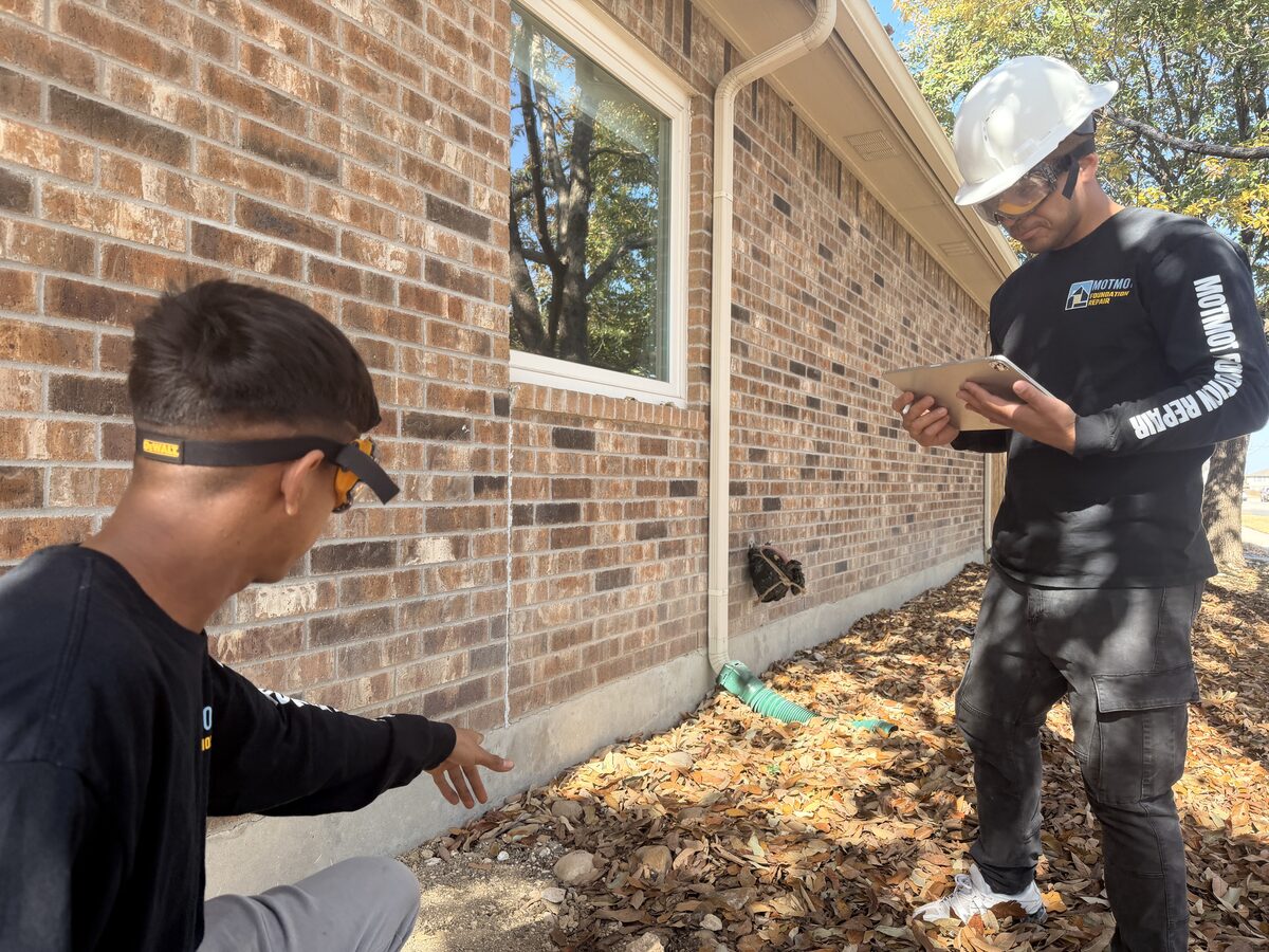 Technicians documenting cracked brick veneer at the slab line during a foundation inspection
