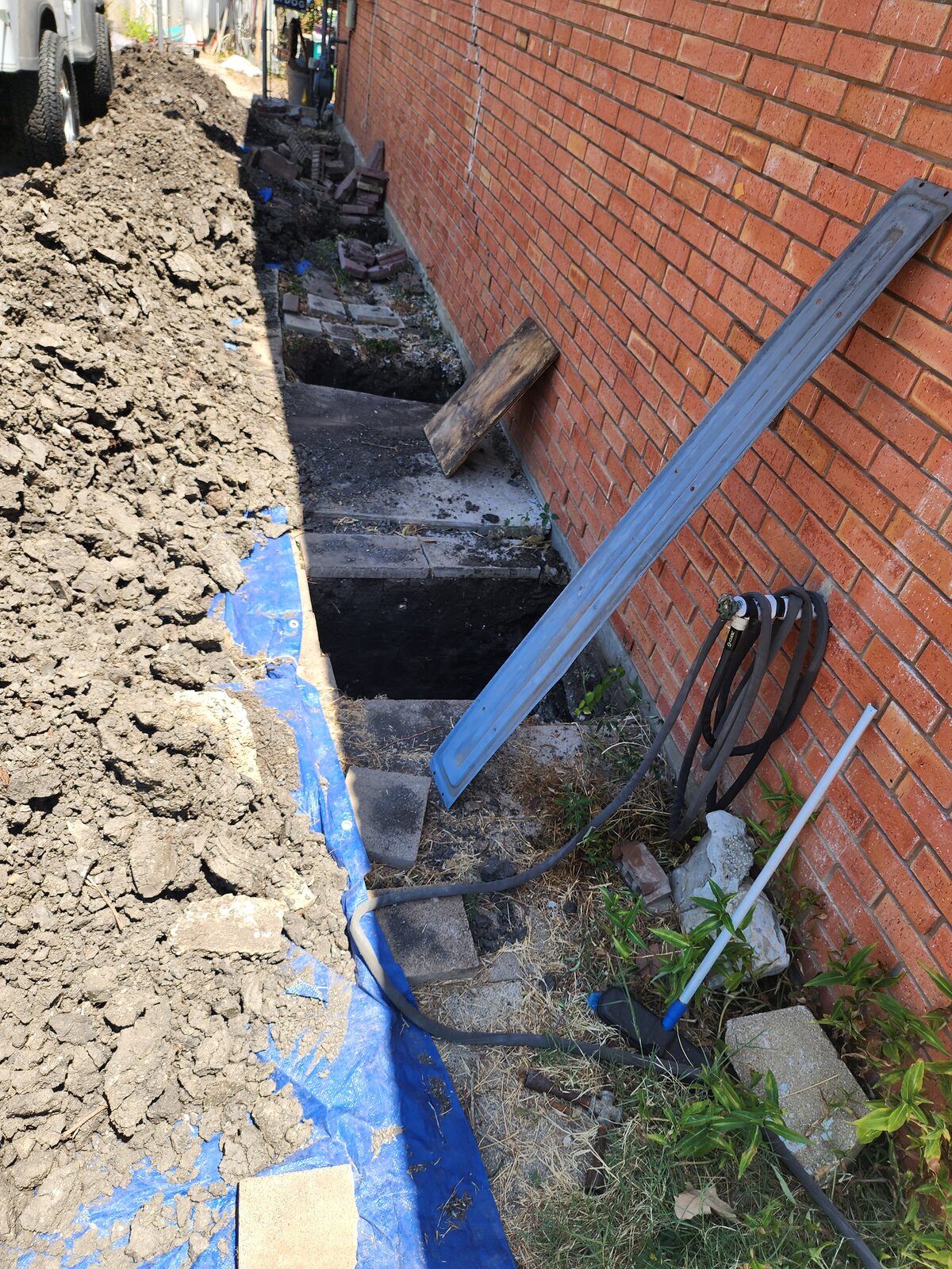 Open trench exposing the concrete footing along a brick wall during foundation underpinning