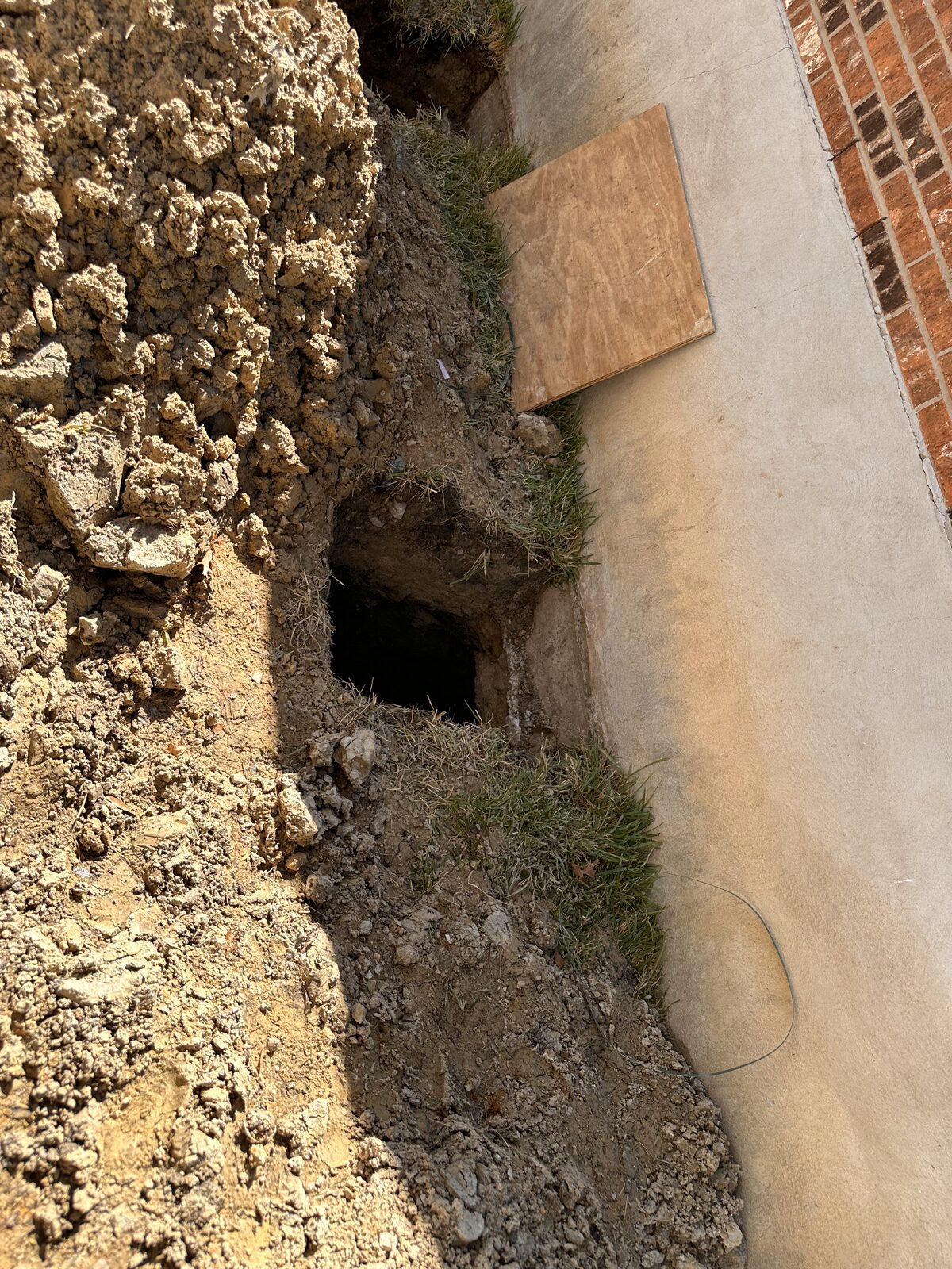 Excavation trench revealing a tunnel dug beneath a stucco-coated stem wall for foundation access on an Austin job