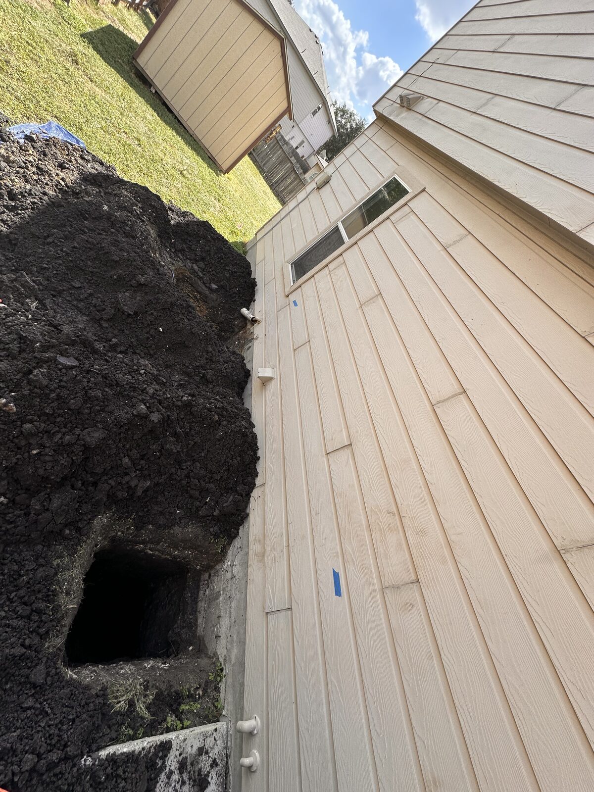 Looking down a foundation wall at a tunnel access hole dug in dark clay soil for under-slab repair