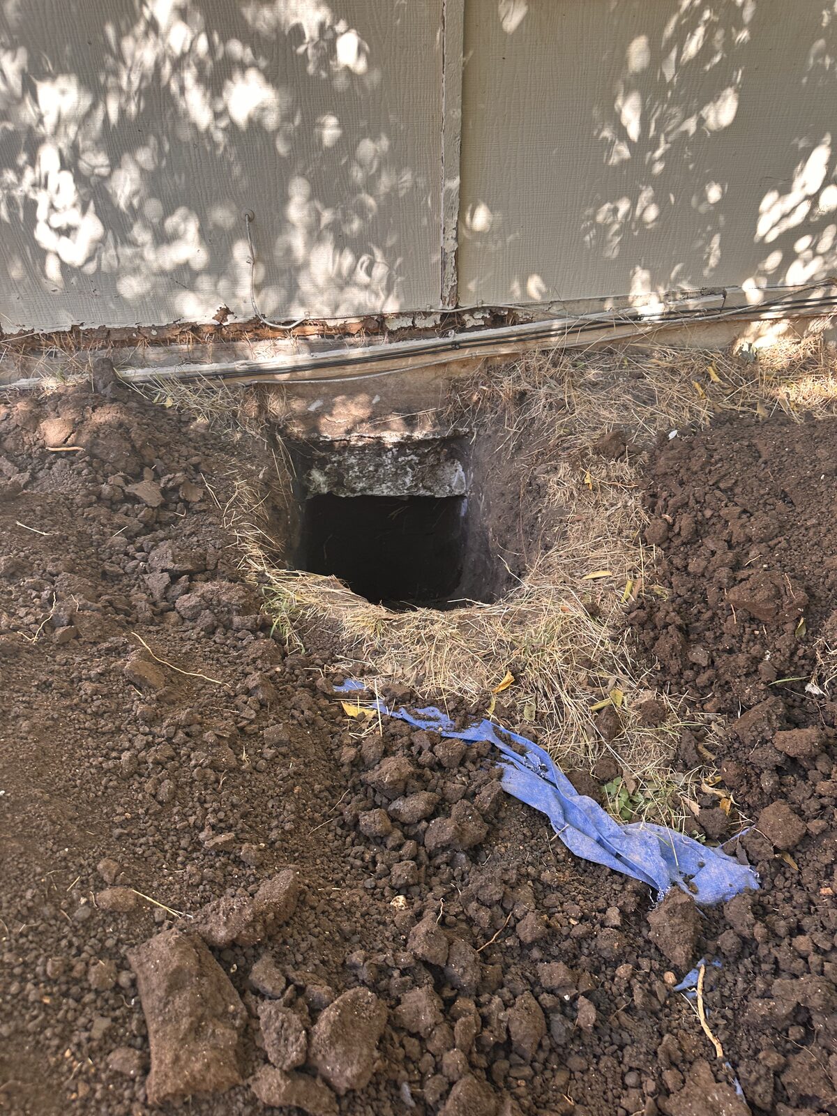 Tunnel access hole dug beneath a stucco foundation wall with spoil piled alongside during repair