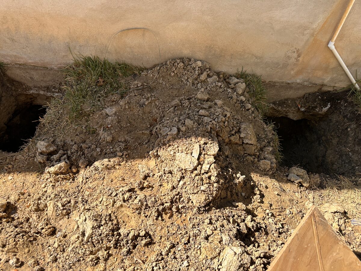 Close view of a cavity tunneled beneath a footing during foundation repair, spoil mounded above