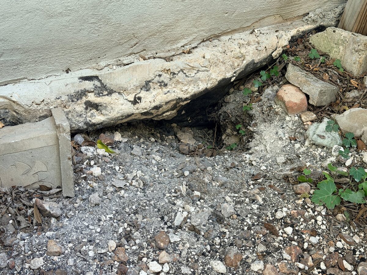Broken slab corner with soil washed out from underneath, leaving a hollow under the foundation edge