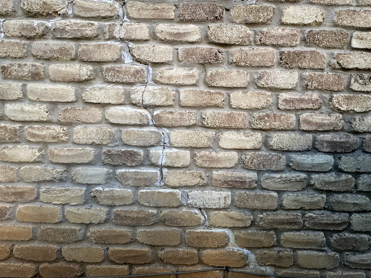 Vertical crack running through tan brick veneer and mortar joints, an exterior sign of foundation settlement