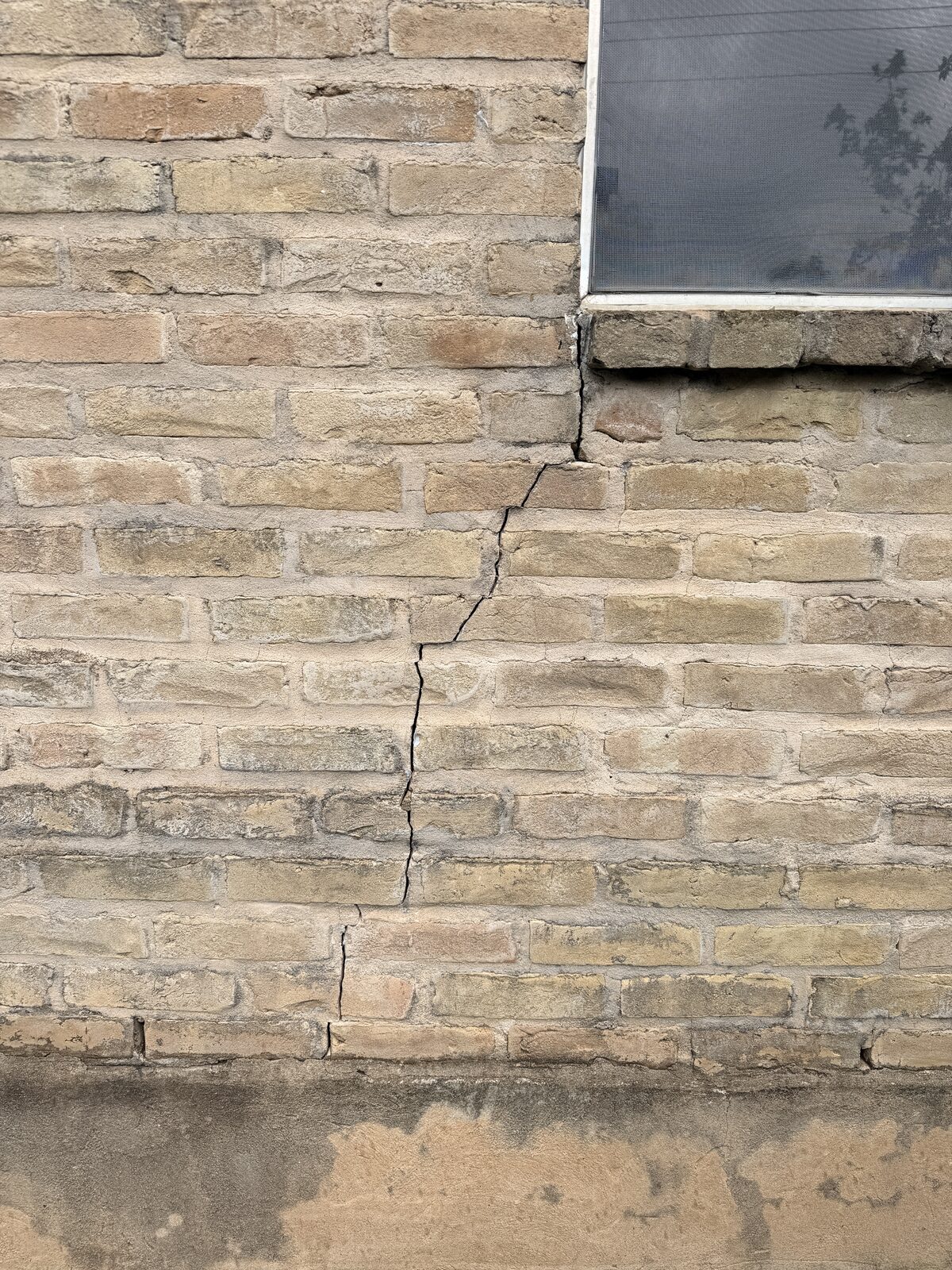 Vertical crack running from a window sill down a cream brick wall to the stem wall, a sign of foundation settlement