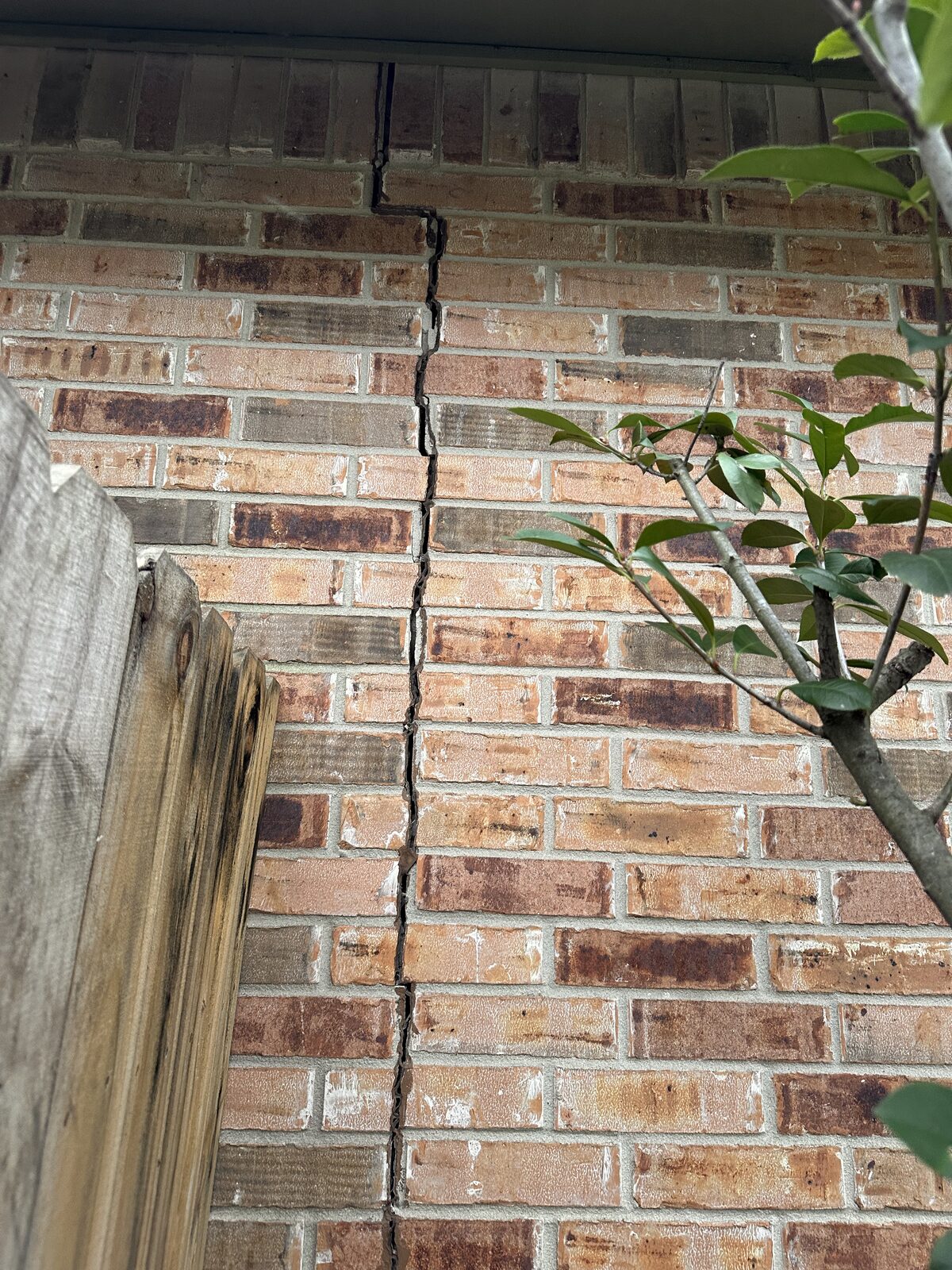 Vertical crack at the corner of a brick home near the fence line, documented during a foundation inspection