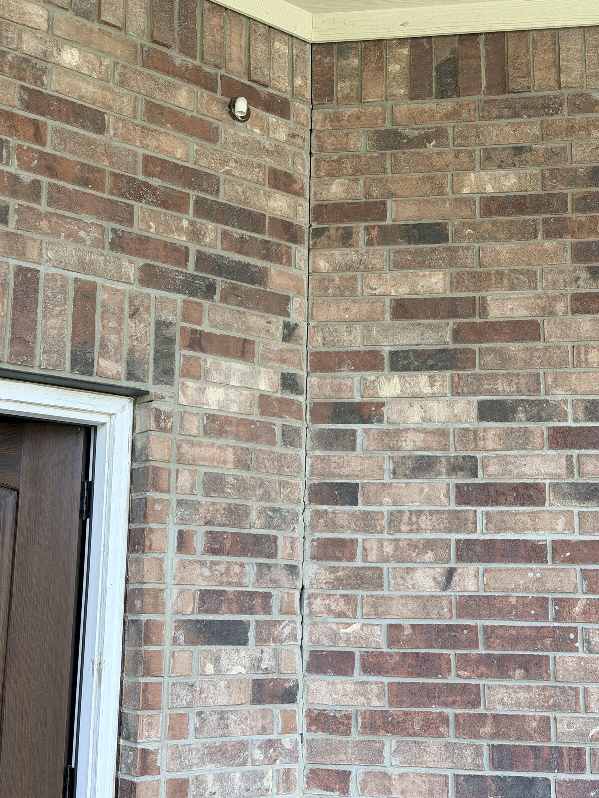 Vertical crack at the brick veneer entry corner of a home, the kind a buyer's inspector flags