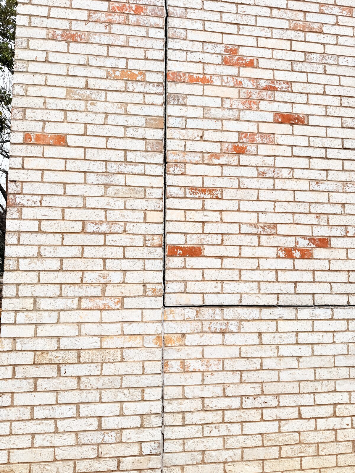 Straight vertical separation crack running through a light-colored brick wall