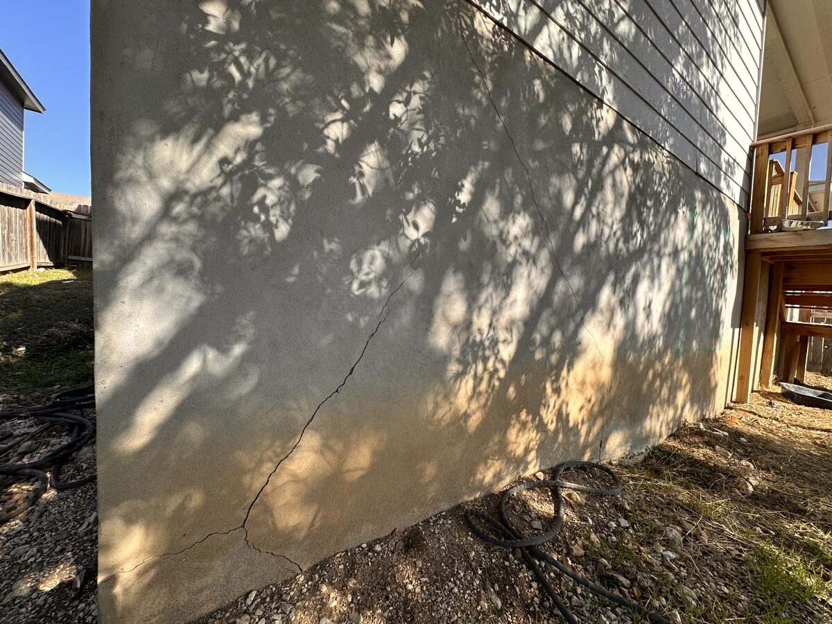 Vertical crack in a stucco-finished stem wall along the side of a house, a sign of foundation settlement