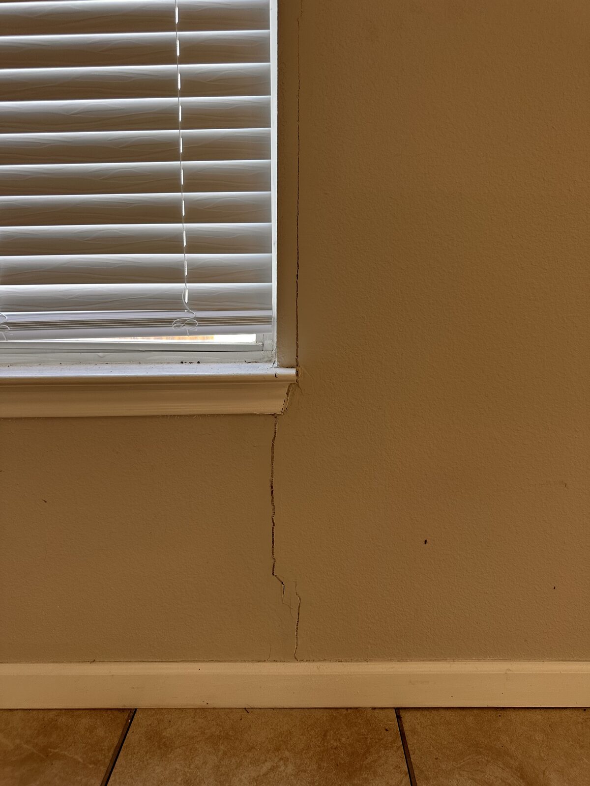 Vertical drywall crack running from a window sill down to the baseboard in a settling home