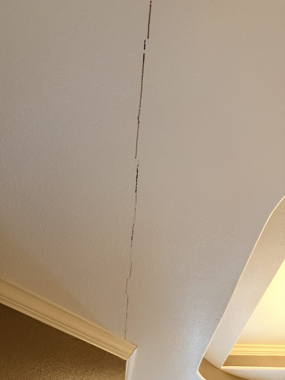 Tall vertical drywall crack on a two-story living room wall, interior evidence of slab foundation settlement