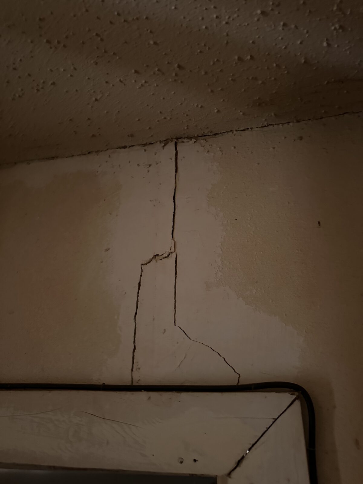 Long vertical plaster crack down a wall corner above bedroom furniture in a settling home