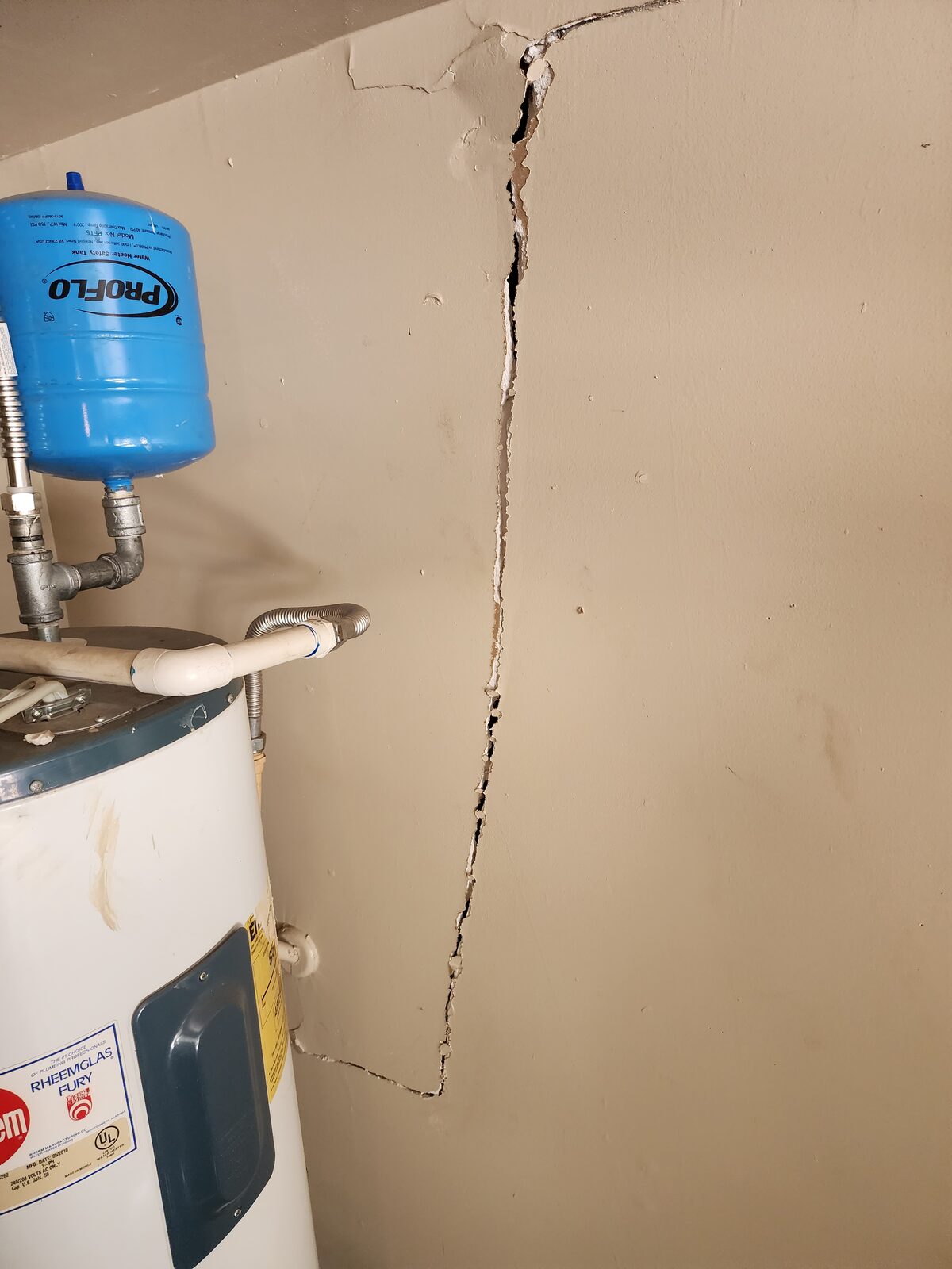 Close-up of a wide vertical wall crack beside a water heater, an interior clue of foundation settlement