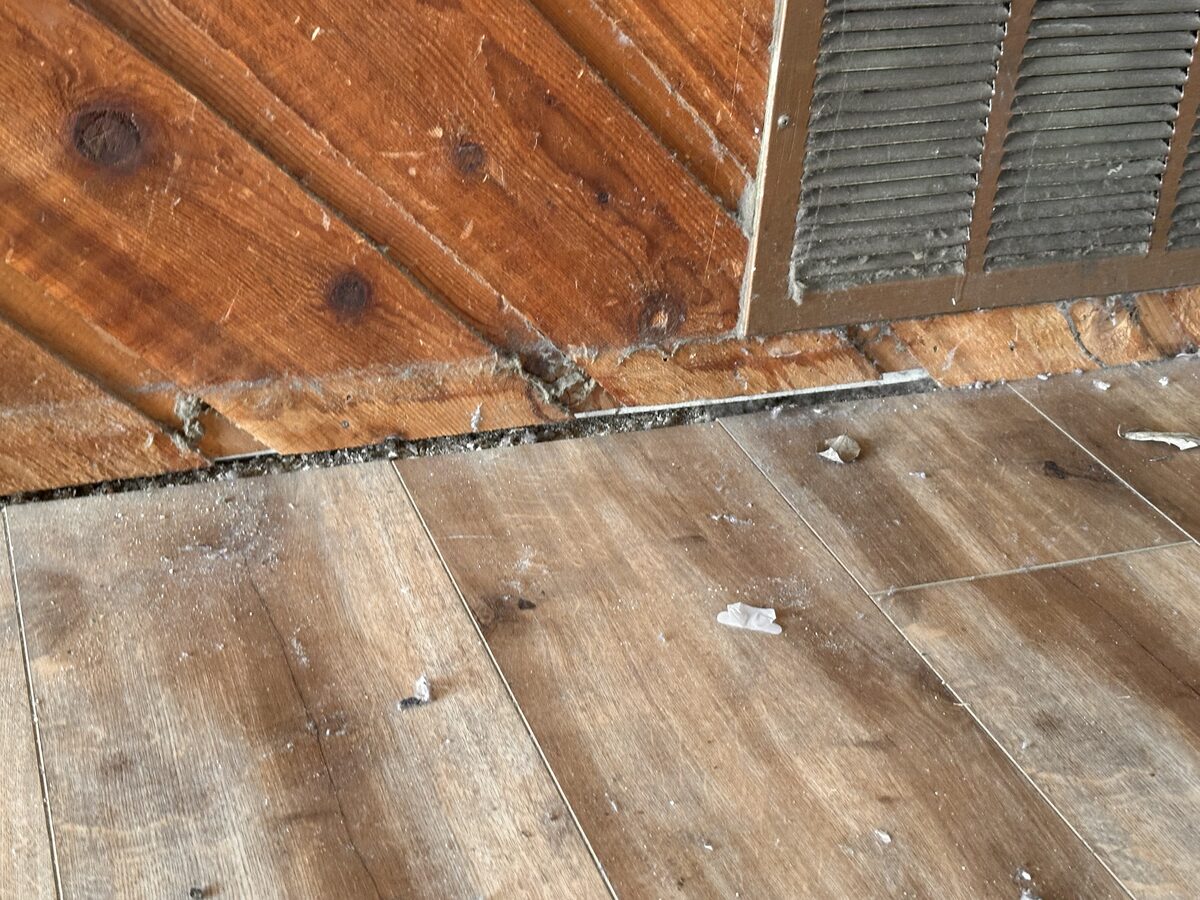 Gap opening between a wood-paneled wall and the floor near air vents in a settling pier-and-beam home
