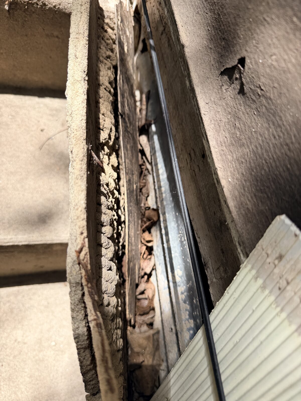 Open joint at the sill line showing a weathered wood sill board and debris