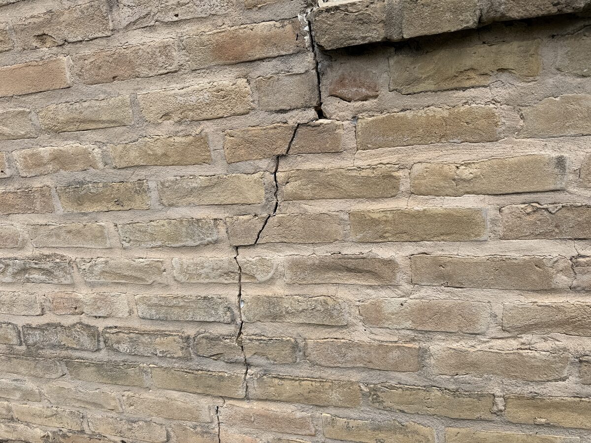Wide vertical crack splitting brick at a wall corner beneath the eave of a settling home